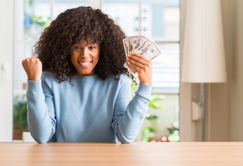 African american woman holding dollar bank notes screaming proud and celebrating victory and success very excited, cheering emotion