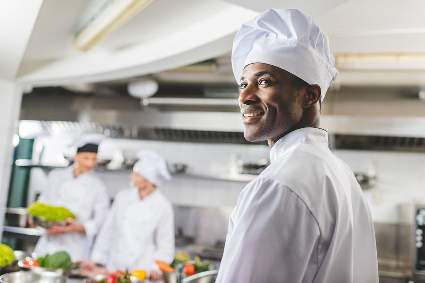 smiling african american chef looking away at restaurant kitchen